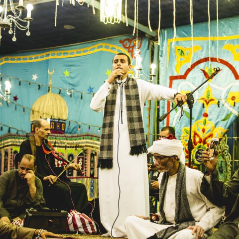 A group of people wearing traditional clothes from the Egyptian culture listening to the singer